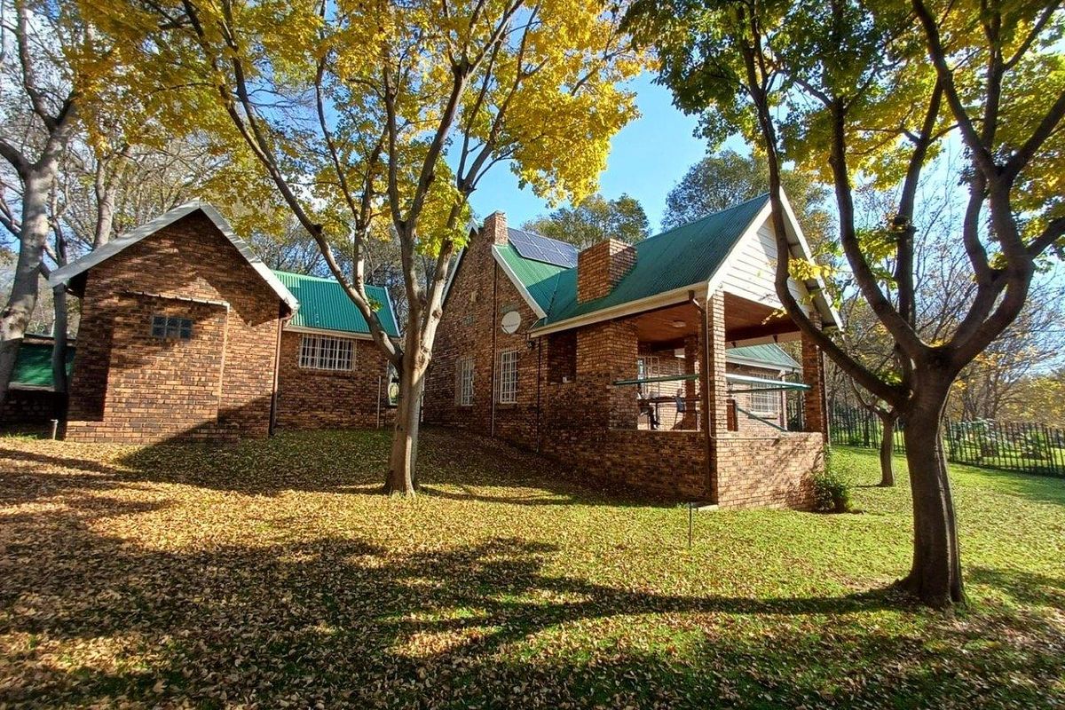 A view of the rear brick facade featuring a covered patio, green metal roofing, and mature trees in a landscaped garden setting.