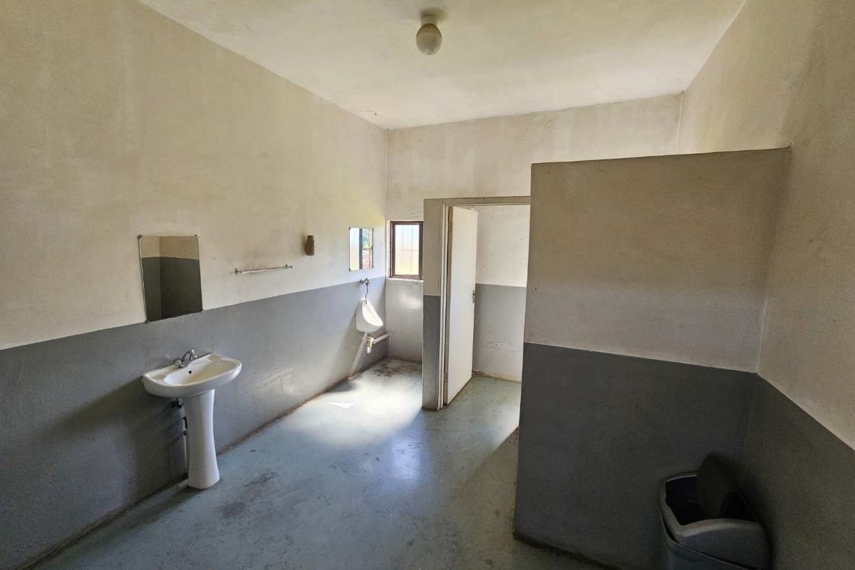 A functional industrial-style bathroom featuring a pedestal basin, a wall-mounted urinal, and a partition wall for privacy.