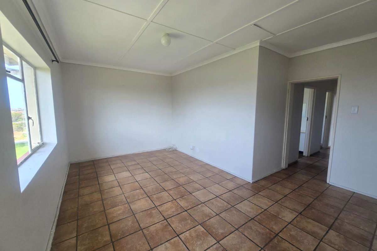 An empty living area featuring tiled flooring, neutral walls, and a large window, offering a blank canvas for renovation or interior design.