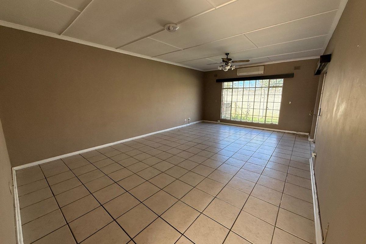 Spacious, empty living area featuring tiled flooring, a ceiling fan, and a wall-mounted air conditioning unit with large windows providing natural light.