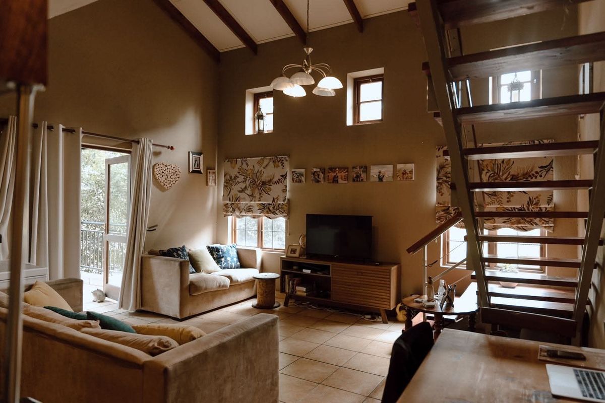 Spacious living room featuring high vaulted ceilings with exposed timber beams, tiled flooring, and a timber staircase leading to an upper level.