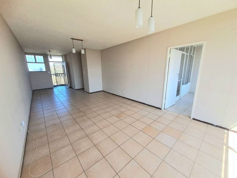 An empty, open-plan living area featuring neutral ceramic floor tiles, pendant lighting, and access to an exterior balcony through a security gate.