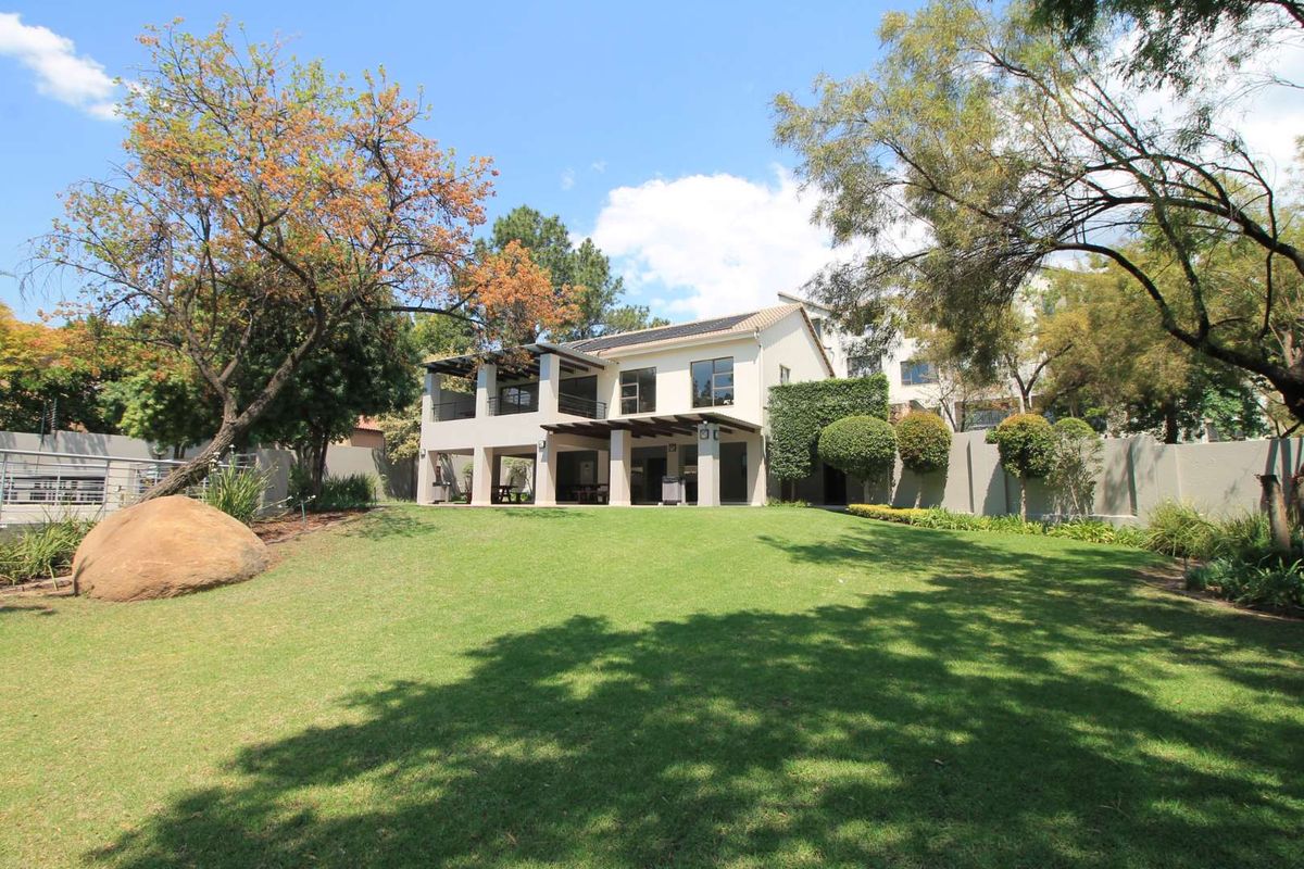 Rear view of the property featuring a spacious lawn, landscaped garden, covered patio, and balcony with solar panels installed on the roof.