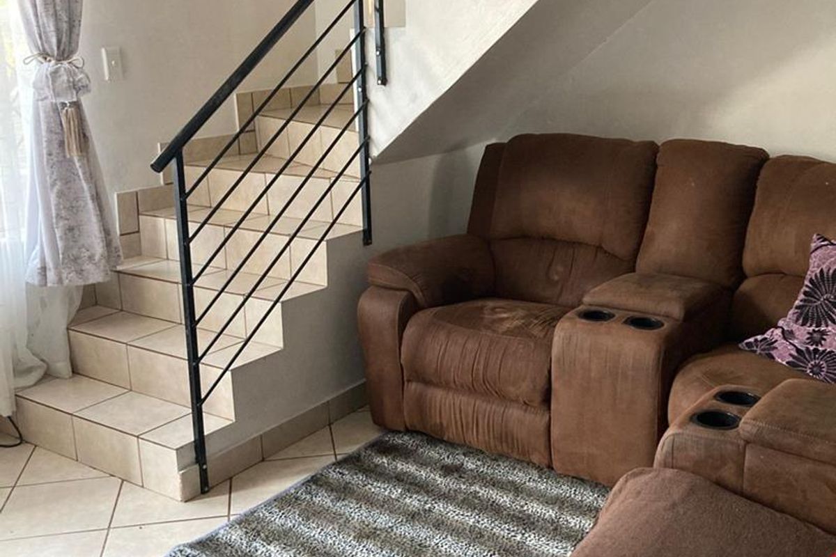 A living area featuring tiled flooring and a staircase with a black metal balustrade, situated under the stairwell.