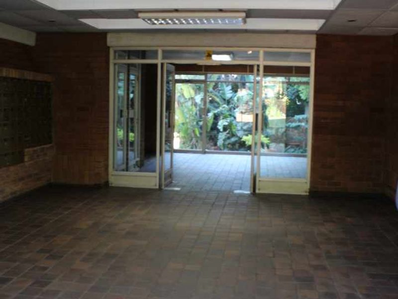 Spacious apartment building entrance lobby featuring brick walls, tiled flooring, and built-in mailboxes, leading out to a garden area.