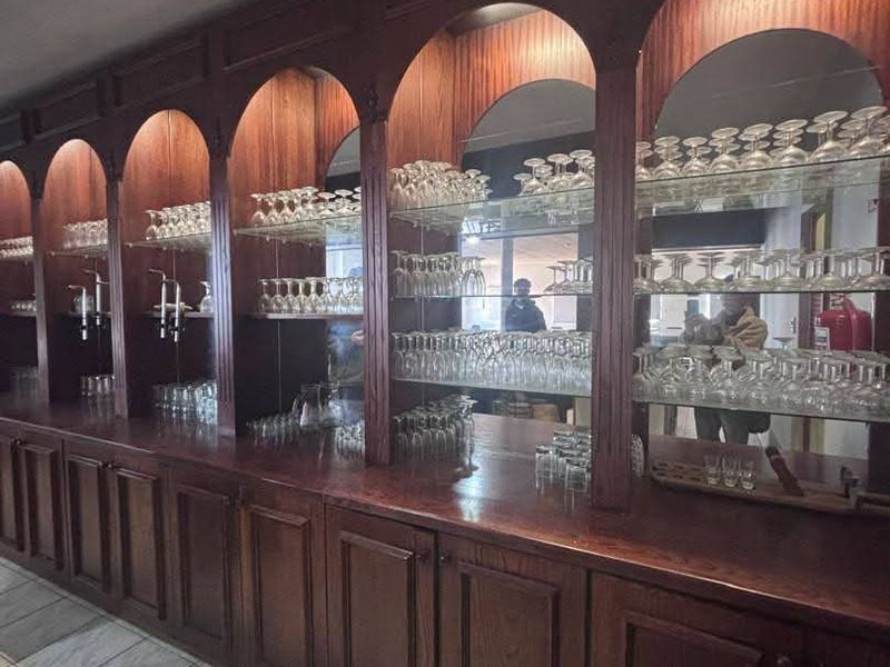 A classic wooden bar area featuring arched display shelving with integrated mirrored back panels and ample storage cabinetry.