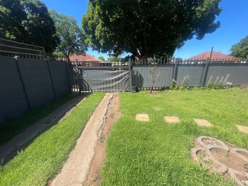 A private garden area featuring a lawn, perimeter fencing, and a metal driveway gate with concrete driveway strips showing signs of wear.
