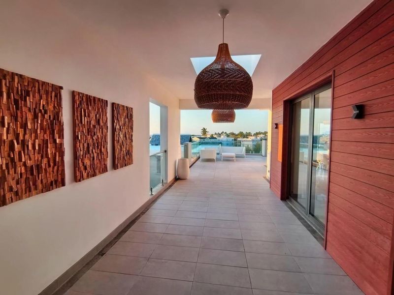 A spacious, modern covered balcony featuring tiled flooring, a glass balustrade, and stylish timber-look wall cladding, offering an open-air transition to the outdoors.