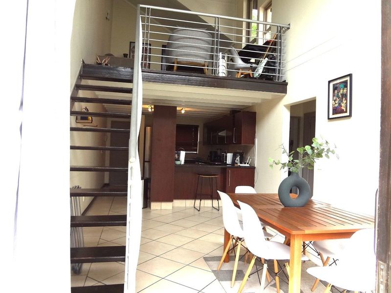 Open plan living area featuring a mezzanine level, metal staircase with stainless steel balustrade, tiled flooring, and a compact kitchen with built-in cabinetry.