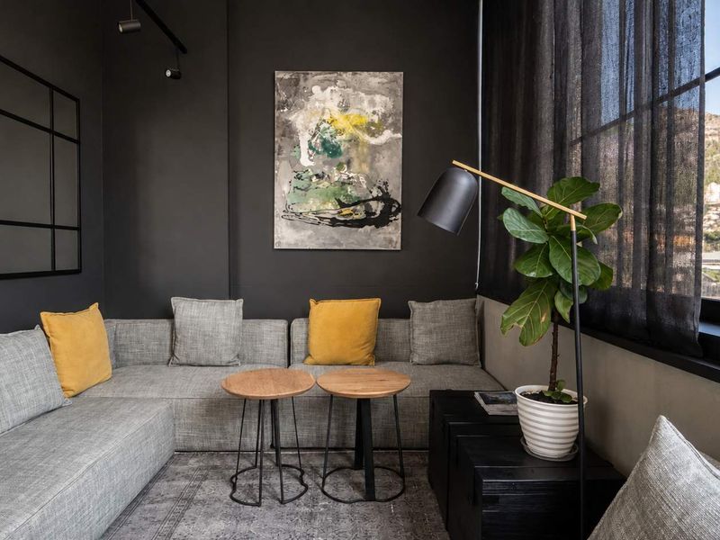 A modern, stylish living area featuring dark charcoal walls, industrial-style steel-framed windows, and recessed track lighting, offering a sophisticated and contemporary aesthetic.