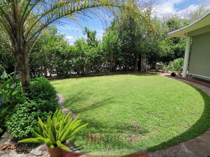 A well-maintained private garden featuring a manicured circular lawn, mature perimeter hedging, and a covered patio area.