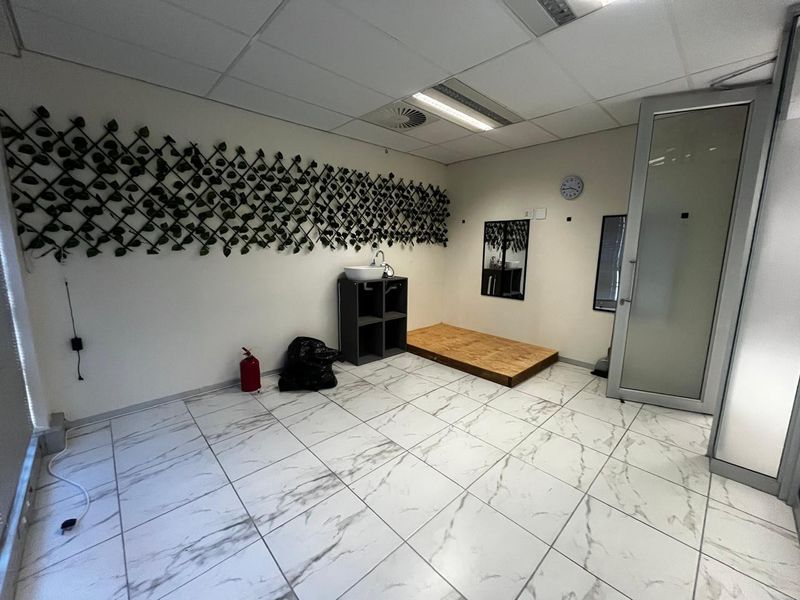 A functional office space featuring marble-look tiled flooring, a suspended ceiling with recessed lighting, and a glass panel door.