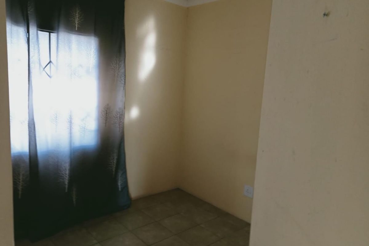 A small, empty bedroom featuring tiled flooring and a window with curtain fixtures, offering a blank canvas for interior design.