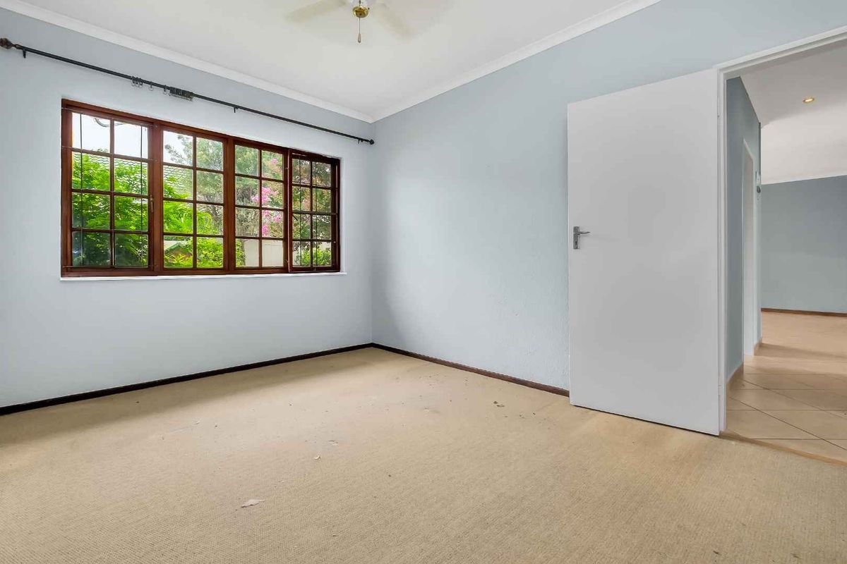 A bright, empty bedroom featuring large wooden-framed windows, neutral wall paint, and carpeted flooring, offering a blank canvas for personalization.