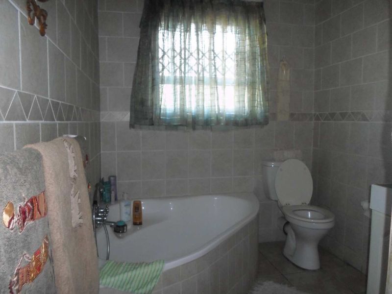 A functional bathroom featuring a corner bathtub, toilet, and neutral ceramic wall and floor tiling.
