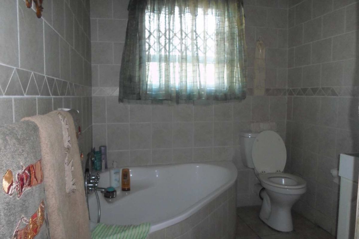 A functional bathroom featuring a corner bathtub, toilet, and neutral ceramic wall and floor tiling.