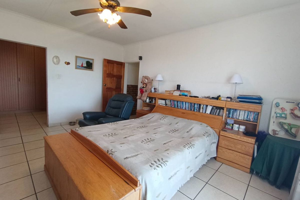 A spacious bedroom featuring tiled flooring, a ceiling fan, and built-in wooden cupboards, offering a functional and comfortable living space.