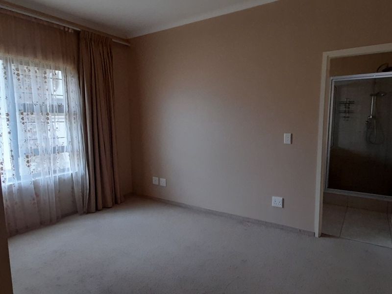 A spacious, empty bedroom featuring neutral carpeting and an attached en-suite bathroom with a shower enclosure.