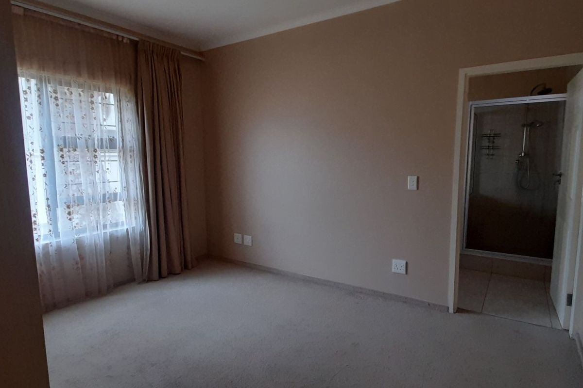 A spacious, empty bedroom featuring neutral carpeting and an attached en-suite bathroom with a shower enclosure.