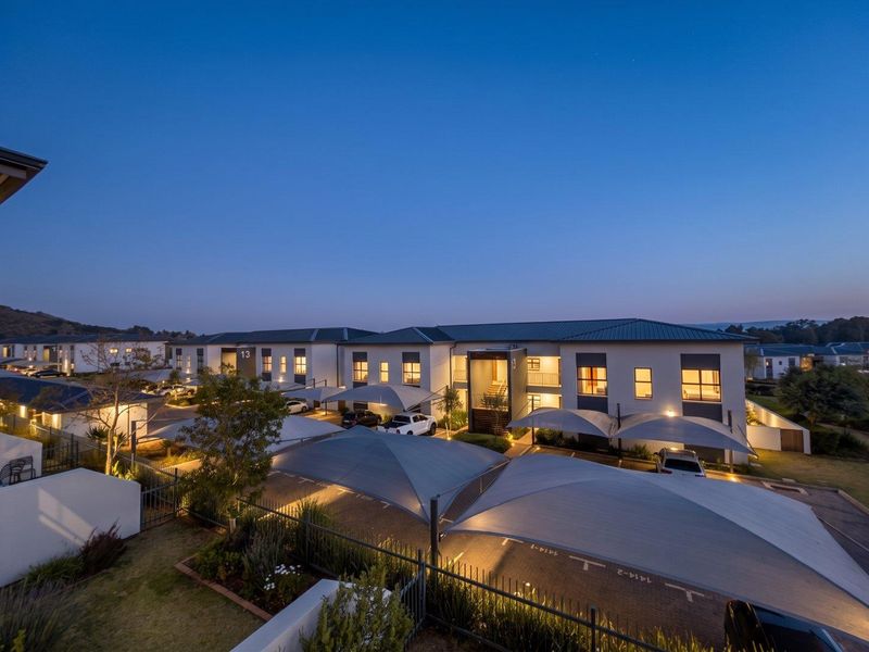 An elevated evening view of an apartment complex featuring modern architecture, paved parking areas with shade-cloth carports, and well-maintained landscaped grounds.