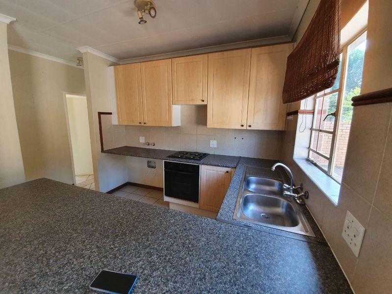 A functional kitchen featuring light wood cabinetry, granite-look laminate countertops, a double stainless steel sink, and a built-in oven with a gas hob.
