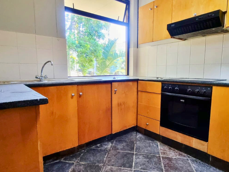 A functional kitchen featuring wooden cabinetry, built-in oven, extractor fan, and tiled backsplash, offering a blank canvas for potential modern updates.