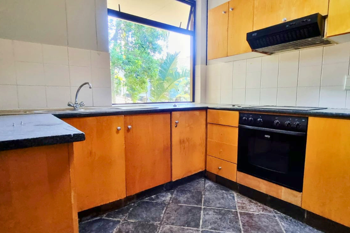 A functional kitchen featuring wooden cabinetry, built-in oven, extractor fan, and tiled backsplash, offering a blank canvas for potential modern updates.