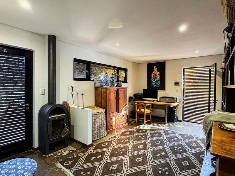 A versatile living space featuring a modern freestanding fireplace, recessed lighting, built-in shelving, and polished concrete flooring with dual access to outdoor areas.