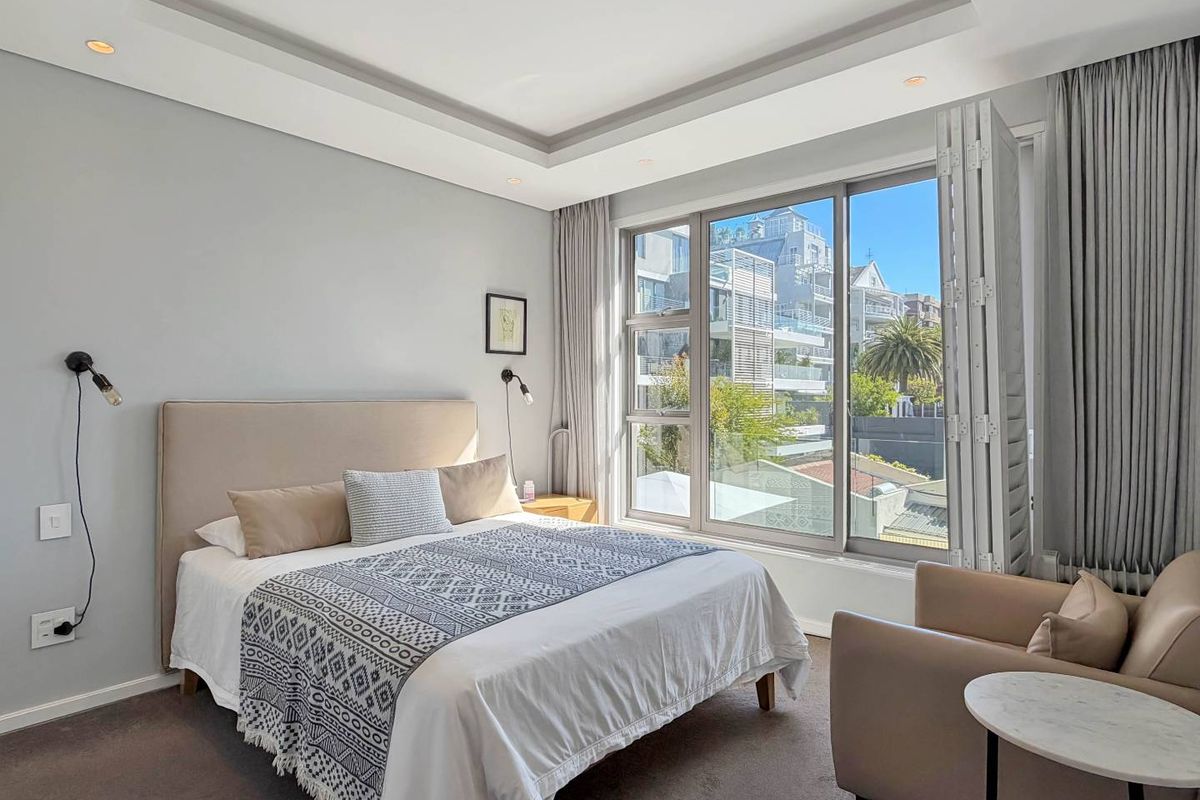 A well-maintained bedroom featuring a recessed ceiling with downlights, carpeted flooring, and large windows with integrated shutters offering natural light and neighborhood views.