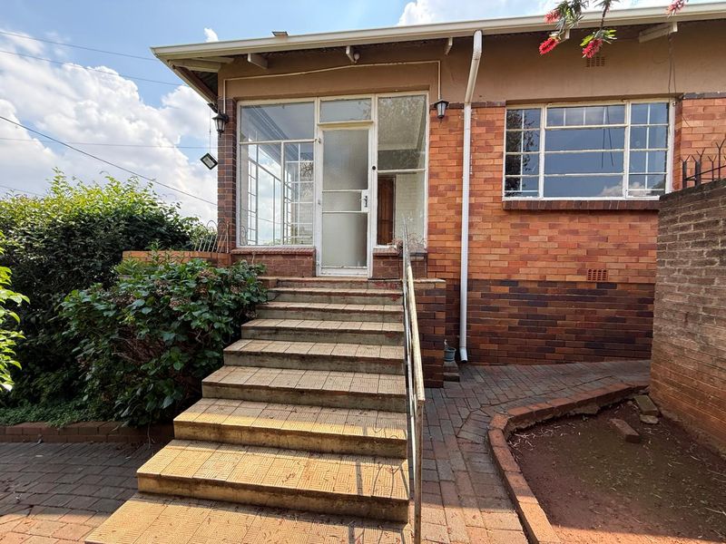 Rear exterior view featuring a brick facade, tiled staircase with metal handrail, and an enclosed porch entrance with steel frame windows.