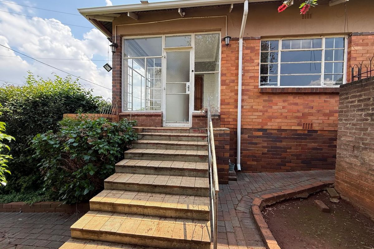 Rear exterior view featuring a brick facade, tiled staircase with metal handrail, and an enclosed porch entrance with steel frame windows.
