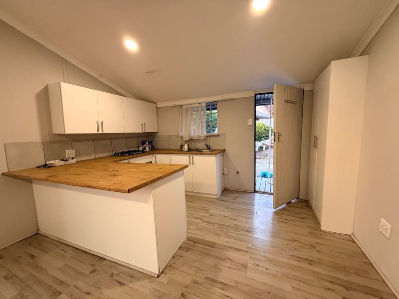 A functional kitchen featuring wooden countertops, built-in cabinetry, a gas hob, and direct access to the rear exterior.