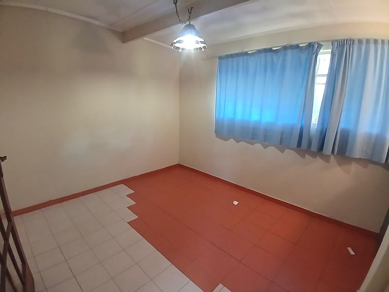 An empty bedroom featuring mismatched floor tiles and a central ceiling light fixture, offering a blank canvas for renovation.