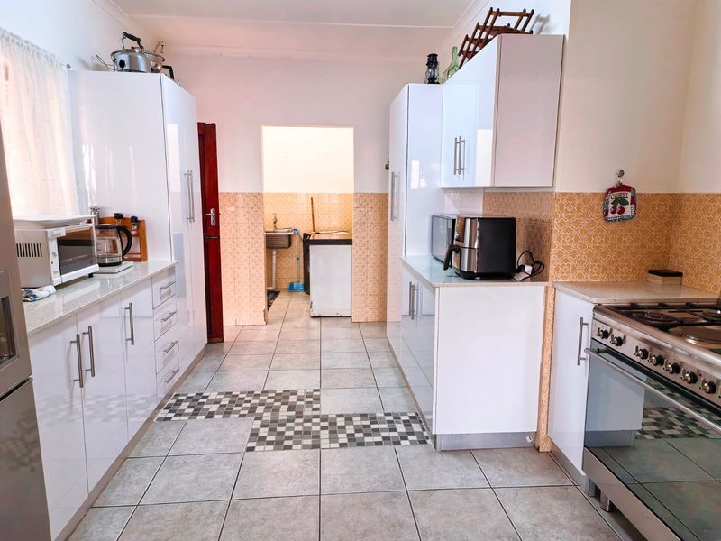 A functional kitchen featuring white high-gloss cabinetry, stone countertops, a gas stove, and tiled flooring, with an adjacent scullery area visible.