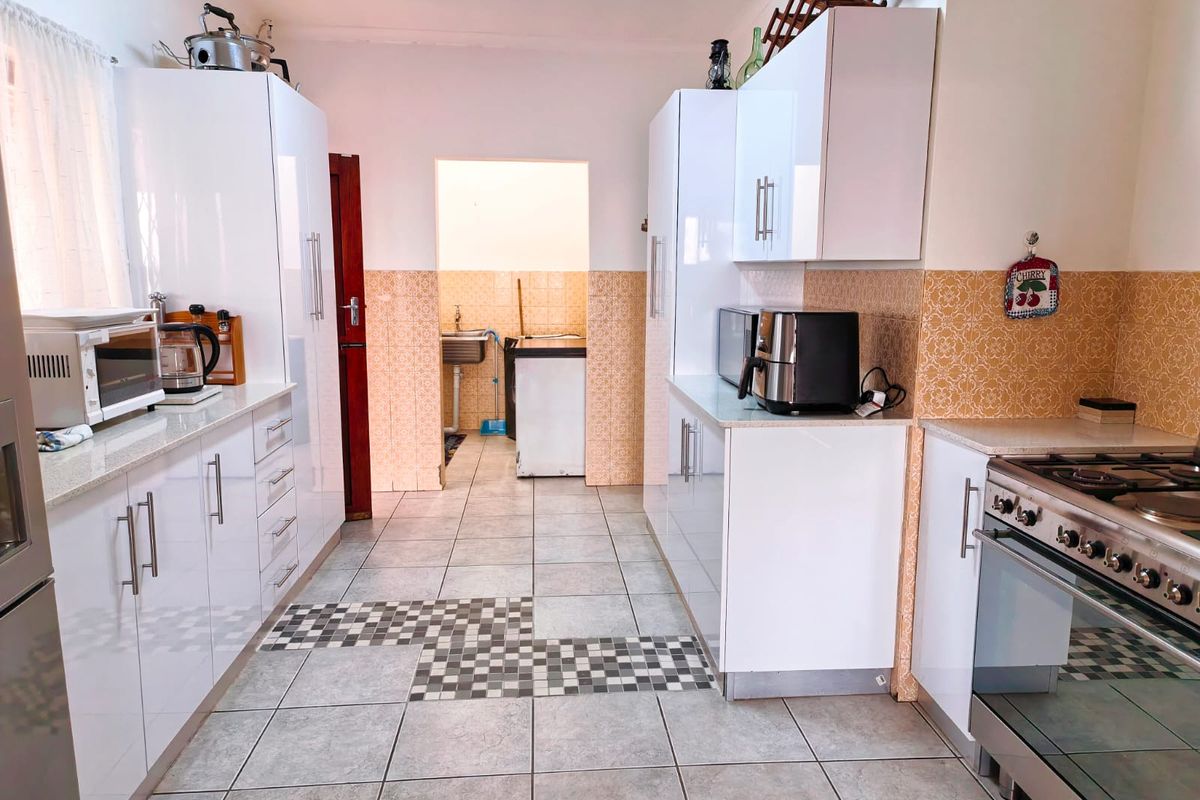A functional kitchen featuring white high-gloss cabinetry, stone countertops, a gas stove, and tiled flooring, with an adjacent scullery area visible.