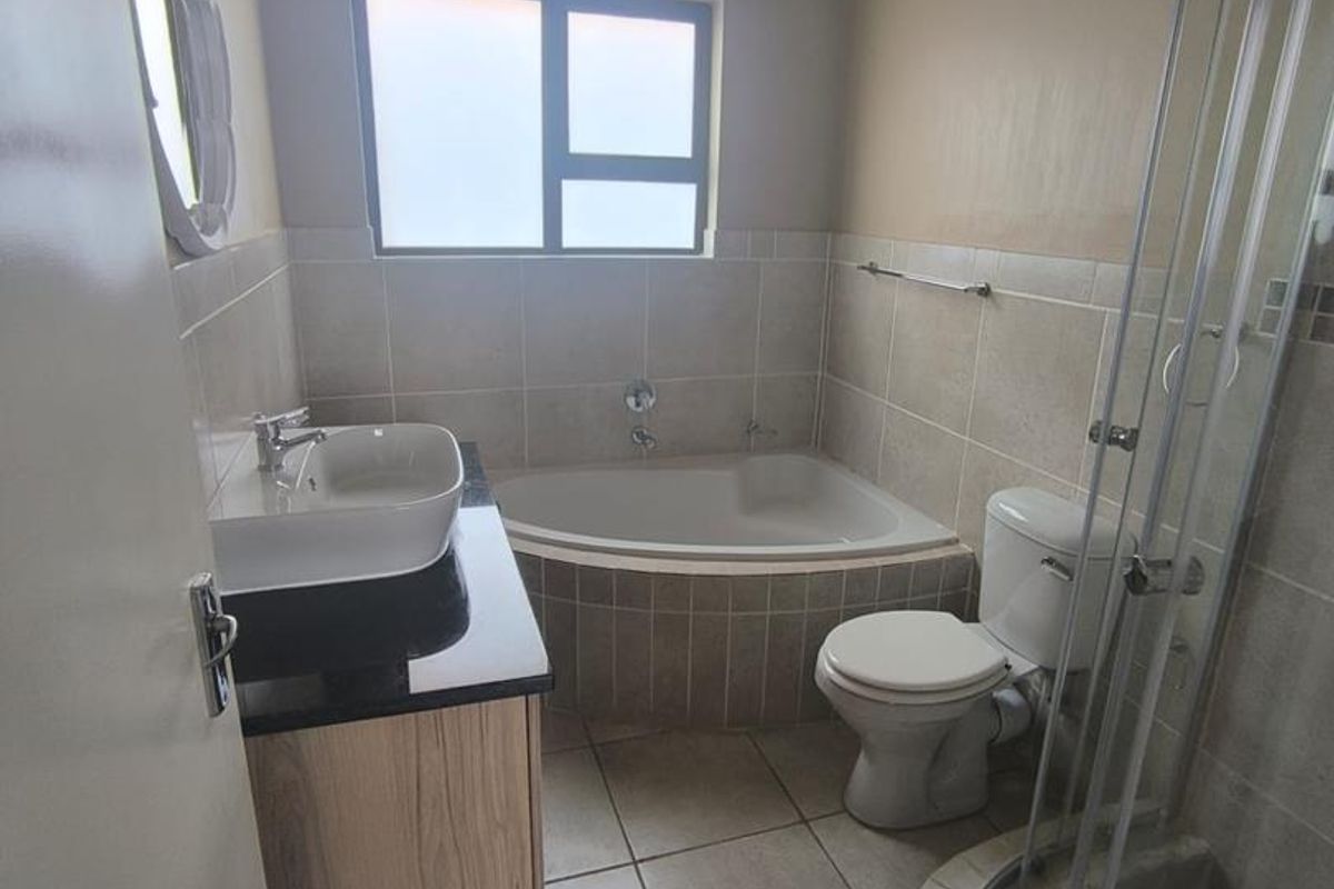 A functional bathroom featuring a corner bathtub, separate shower enclosure, vanity with basin, and toilet, finished with neutral floor and wall tiling.