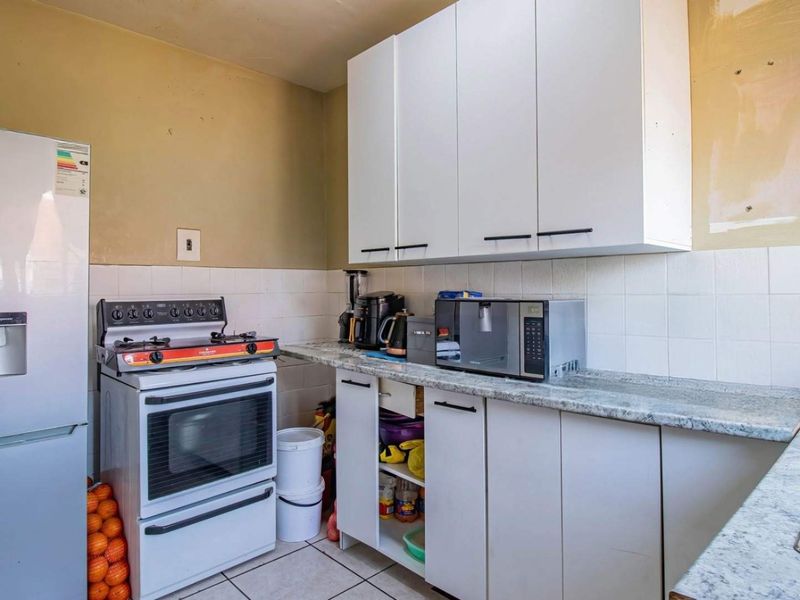 A functional kitchen featuring white cabinetry, a granite-look laminate countertop, tiled backsplash, and a double bowl sink, requiring some cosmetic updates.