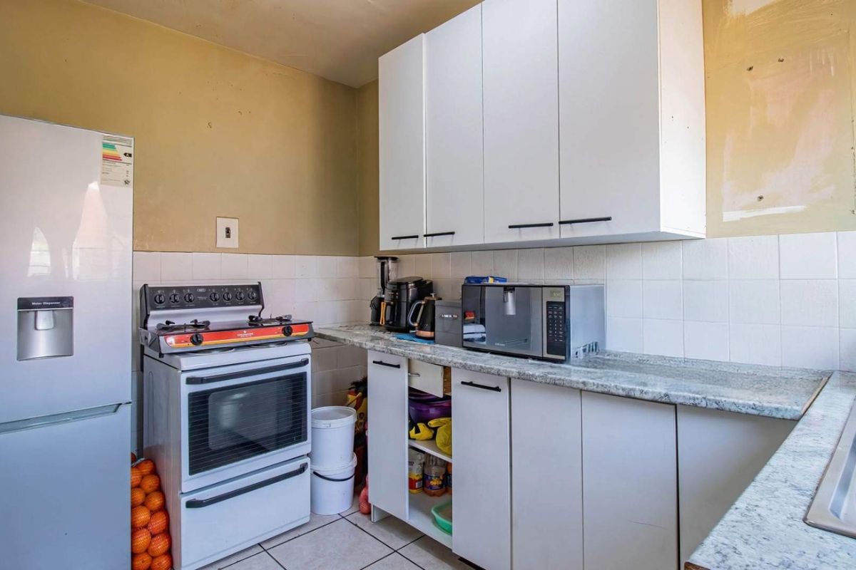 A functional kitchen featuring white cabinetry, a granite-look laminate countertop, tiled backsplash, and a double bowl sink, requiring some cosmetic updates.