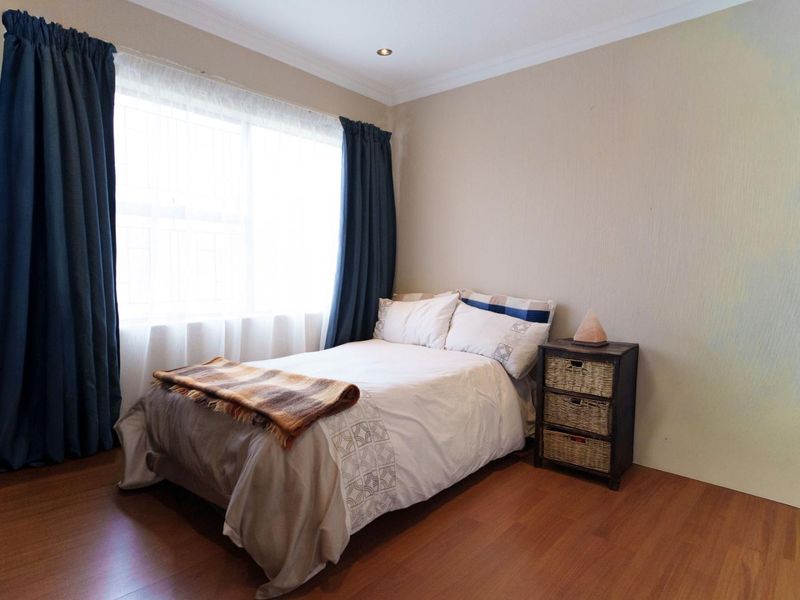A well-lit bedroom featuring warm-toned laminate flooring, coved cornicing, and recessed downlighting, providing a comfortable and functional living space.