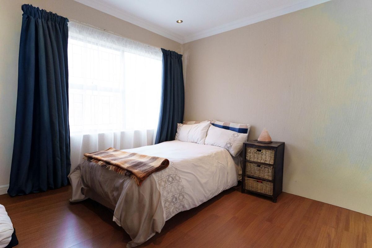 A well-lit bedroom featuring warm-toned laminate flooring, coved cornicing, and recessed downlighting, providing a comfortable and functional living space.