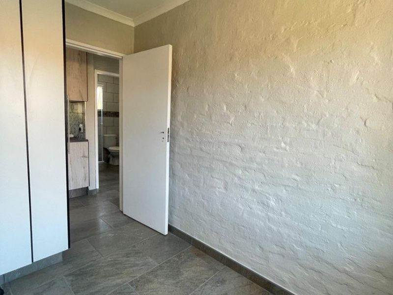 A clean, empty hallway featuring textured brick walls, tiled flooring, and built-in storage cupboards, with a view leading into an adjacent bathroom.