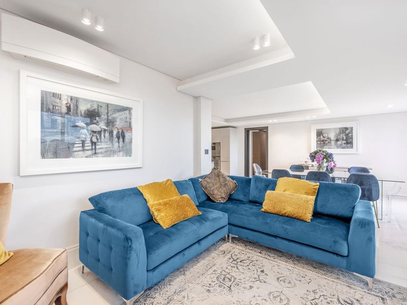 A bright and modern open-plan living and dining area featuring tiled floors, recessed ceiling lighting, and a wall-mounted air conditioning unit.
