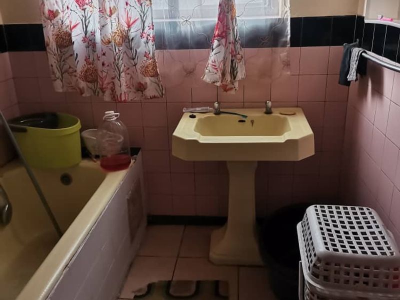 A dated bathroom featuring a pedestal washbasin and built-in bathtub with original ceramic wall tiling.