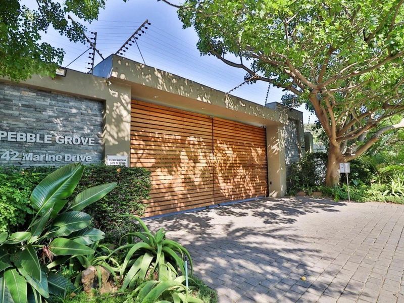 The secure entrance to Pebble Grove townhouse complex featuring a timber slat gate, stone cladding, and electric fencing.