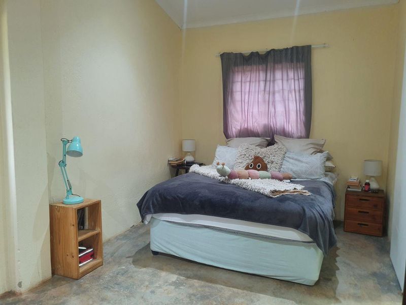 A bedroom featuring concrete flooring, a window with security bars, and coved ceiling details, requiring cosmetic updates to improve the overall finish.