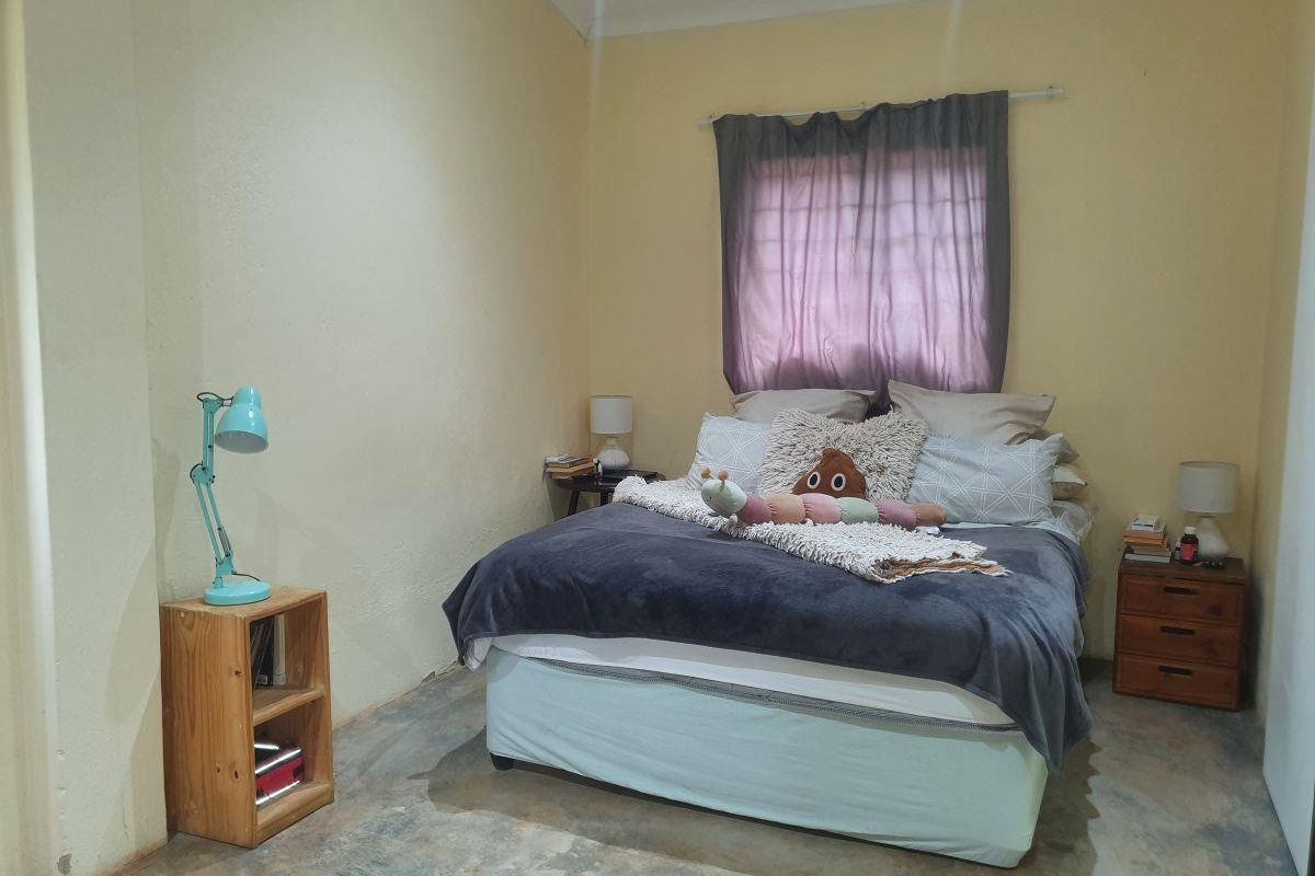 A bedroom featuring concrete flooring, a window with security bars, and coved ceiling details, requiring cosmetic updates to improve the overall finish.