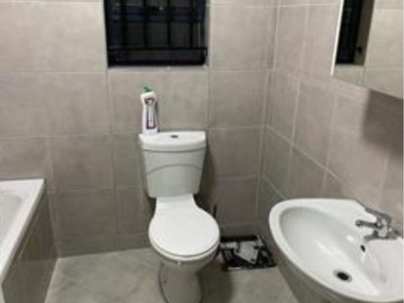 A functional bathroom featuring a pedestal basin, toilet, and bathtub with neutral wall and floor tiling.