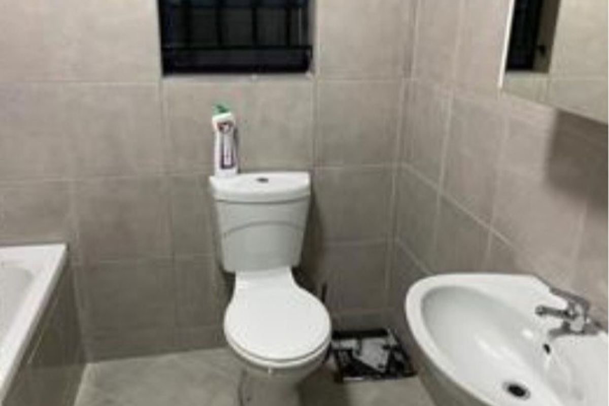 A functional bathroom featuring a pedestal basin, toilet, and bathtub with neutral wall and floor tiling.