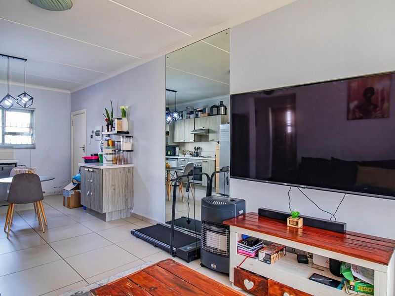 Open-plan living and kitchen area featuring tiled floors, modern cabinetry, integrated appliances, and a large feature mirror, creating a functional and connected living space.