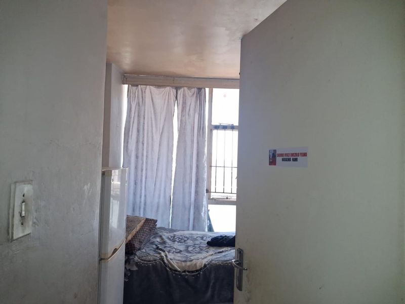 A view into a bedroom featuring security bars on the window and basic interior finishes, showing signs of wear and tear.